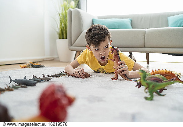 Boy screaming while playing with toy animals on carpet in living room