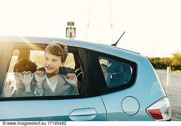 Boy showing head out window car and brother drawing faces at sunrise