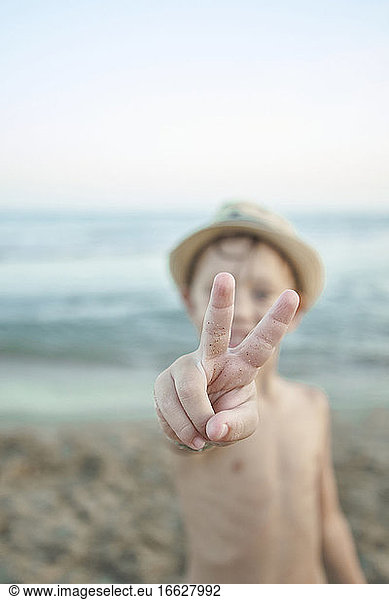 Boy showing peace gesture while standing at beach