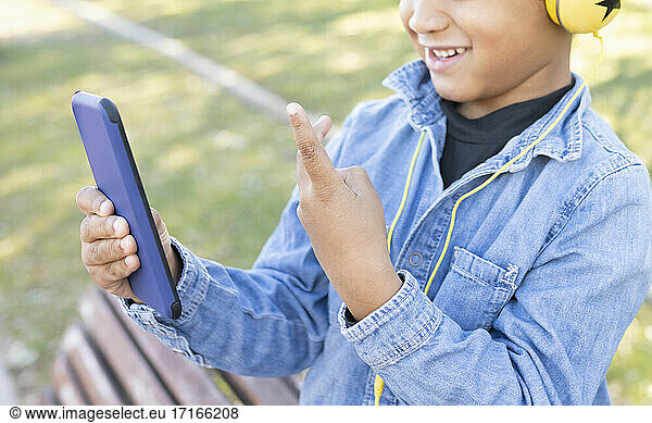 Boy showing peace gesture while using mobile phone at park