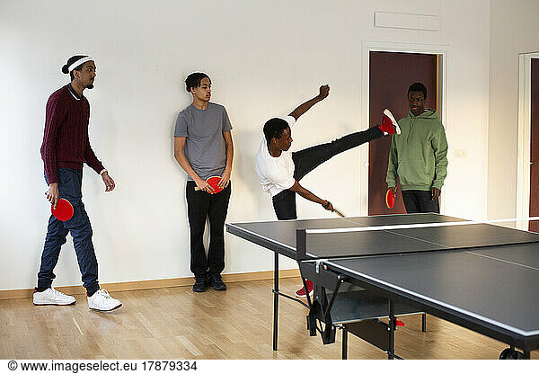 Boy showing stunt to friends while playing table tennis in games room