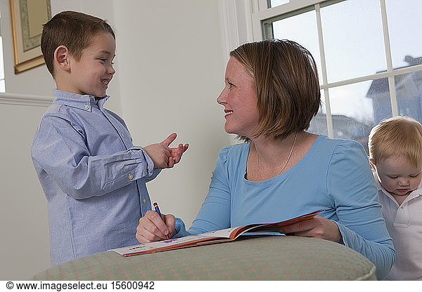 Boy signing the word 'Write' in American Sign Language while communicating with his mother
