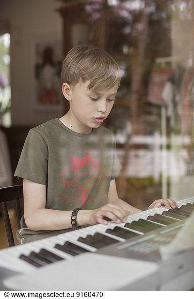 Boy signing while playing piano in house