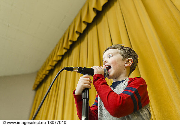 Boy singing on microphone at stage against yellow curtains