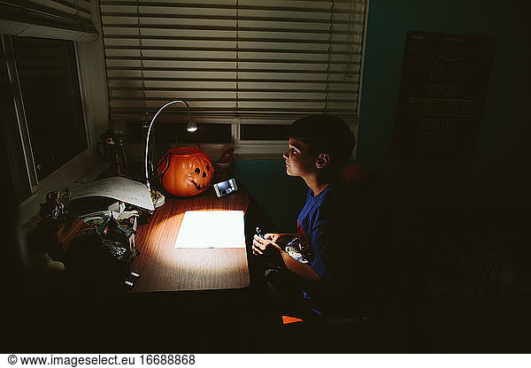 Boy sits in the dark at his desk while on a video call with a friend