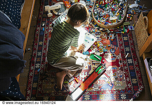 Boy sitting among toys on his bedroom floor in a patch of sunlight