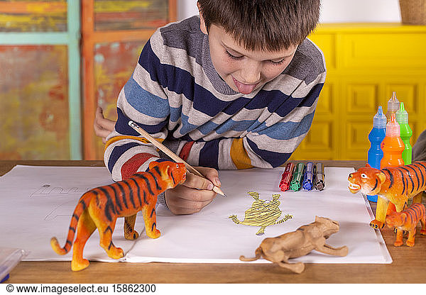 Boy sitting at a table drawing a tiger.
