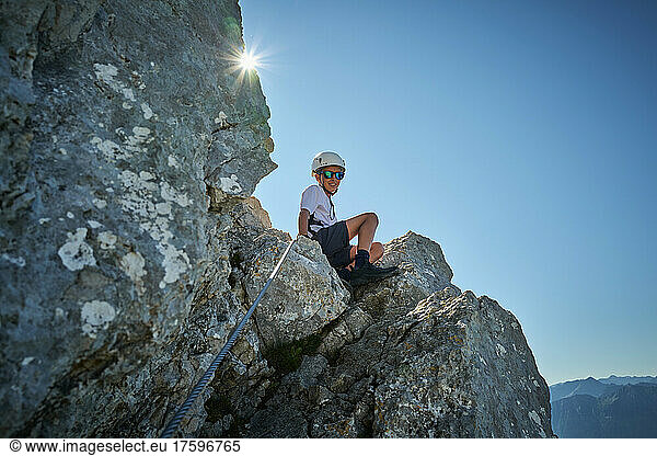 Boy sitting on rock on sunny day