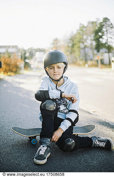 Boy sitting on skateboard at road