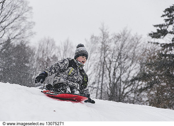 Boy sitting on sled while tobogganing on snow during snowfall