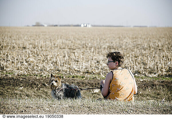 Boy sitting on the side of a country road with his dog.