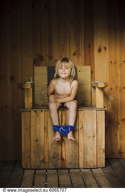 Boy sitting on wooden old fashioned toilet