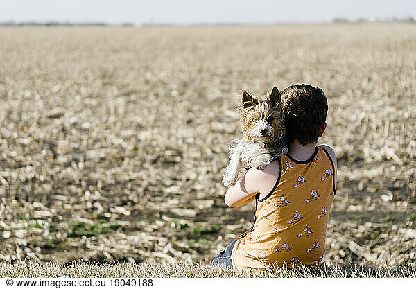 Boy sitting with his dog beside a corn field in the countryside.