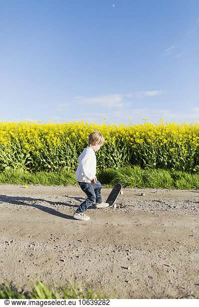 Boy skateboarding on dirt road at oilseed rape field
