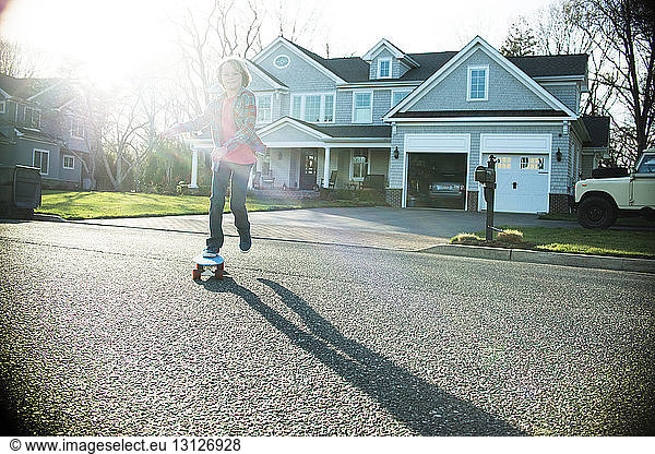 Boy skateboarding on road with house in background