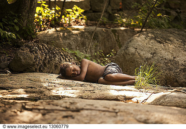 Boy sleeping on rocks in forest
