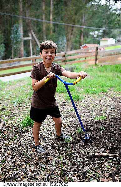 Boy smiling in the yard while he tills soil for a garden