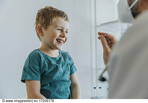 Boy smiling while having nasal swab sitting by doctor at clinic