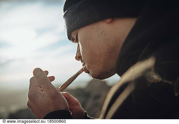 Boy smoking a marijuana joint on top of a mountain during sunset