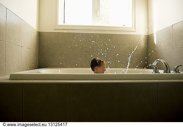 Boy splashing water while taking bath in bathroom