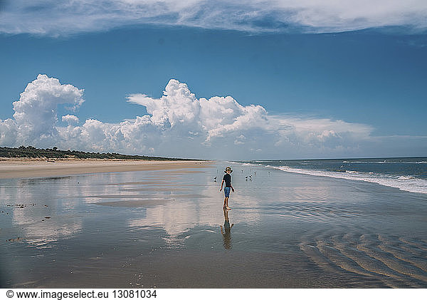 Boy standing at New Smyrna Beach against cloudy sky
