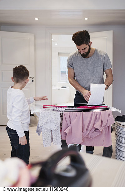 Boy standing by father drying clothes on rack at home