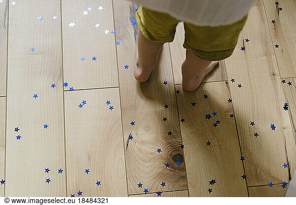 Boy standing on hardwood flooring with star shaped confetti