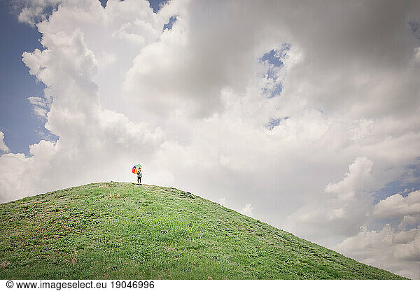 Boy standing on hill with umbrella