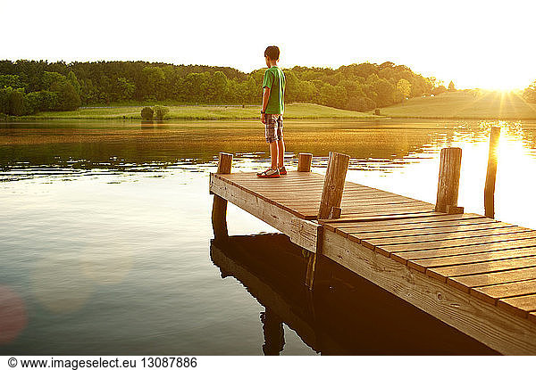 Boy standing on jetty over lake during sunny day