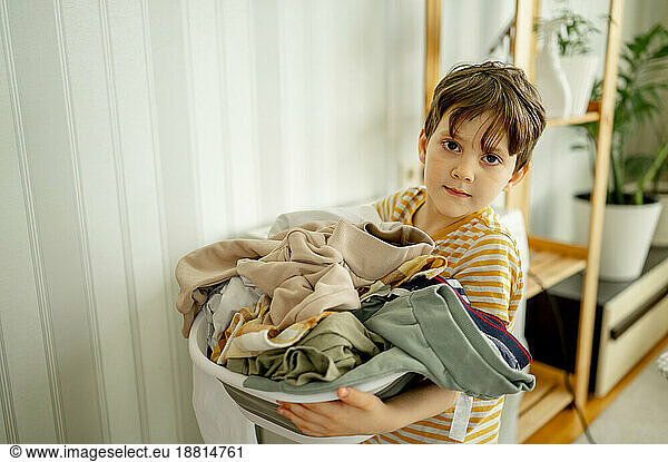 Boy standing with dirty clothes in laundry basket at home