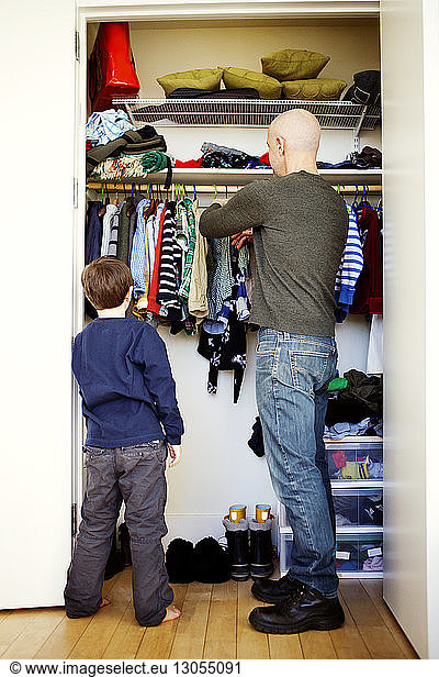 Boy standing with father removing clothes from wardrobe