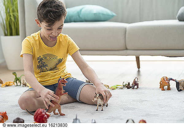 Boy sticking out tongue while playing with toy animals on carpet at home