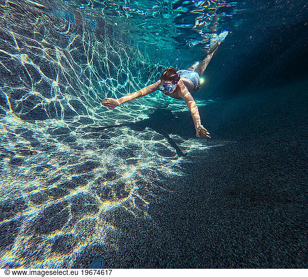 Boy swims in sunshine underwater in a swimming pool