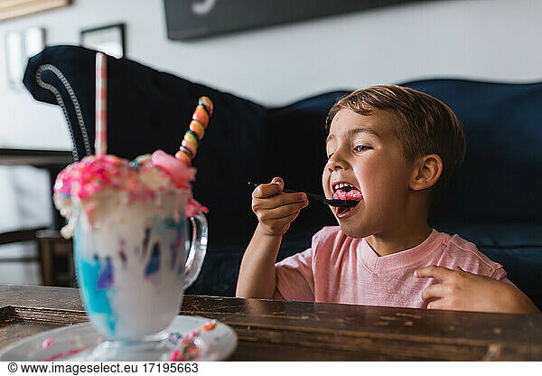 Boy taking a bite of the candy from a colorful milk shake.