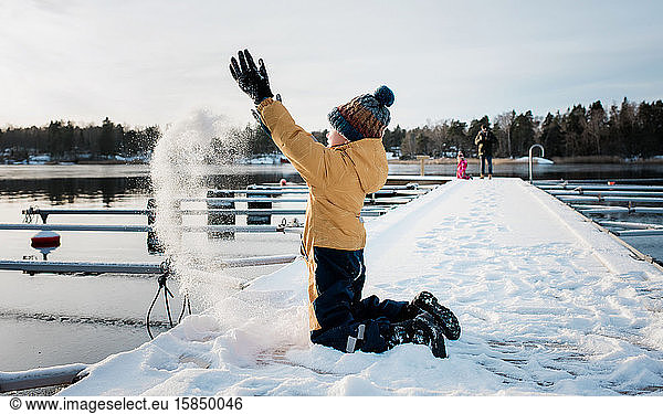 boy throwing snow up in the air whilst playing by the water in Sweden