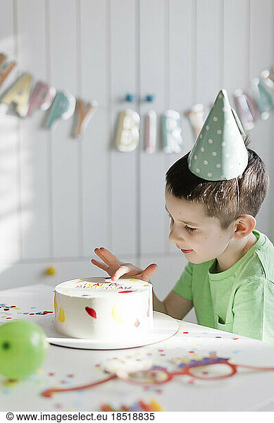 Boy touching birthday cake on table at home