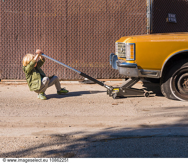 Boy using car jack to raise car
