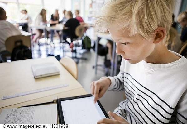 Boy using digital tablet at desk in classroom