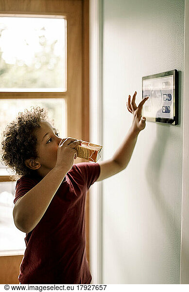 Boy using home automation mounted on wall while drinking juice