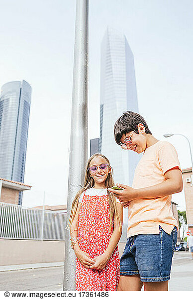 Boy using mobile phone while standing with friend in city