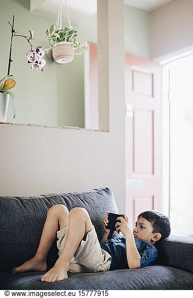 Boy using phone while lying on sofa at home