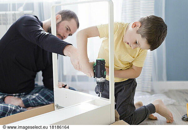 Boy using power screwdriver on table by father at home