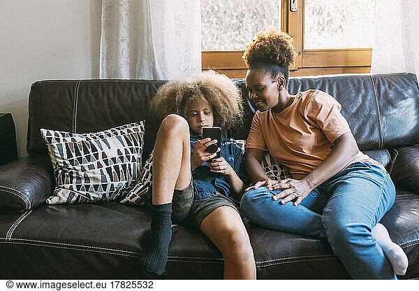 Boy using smart phone sitting with mother on sofa at home