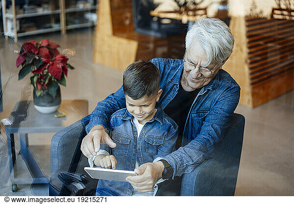 Boy using tablet PC sitting with grandfather at home