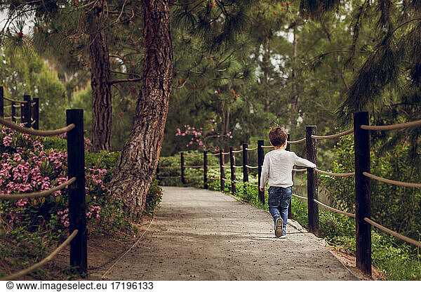 Boy walking down a path next to a rope rail.