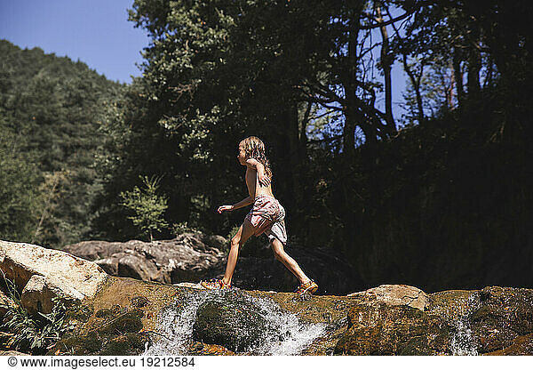 Boy walking near river in forest on sunny day