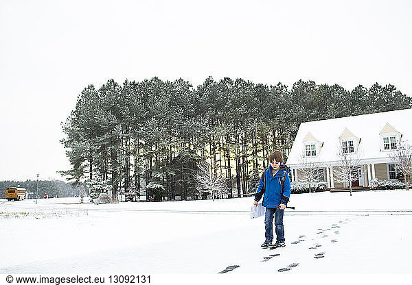 Boy walking on snow covered field against clear sky