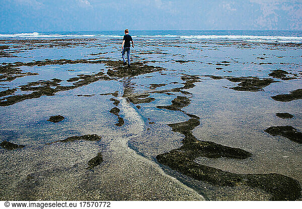 Boy walking out to sea on a path of sand through tide pools