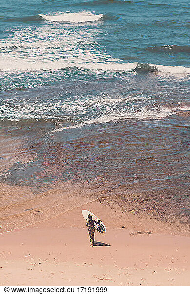 Boy walking towards the ocean carrying his surfboard.