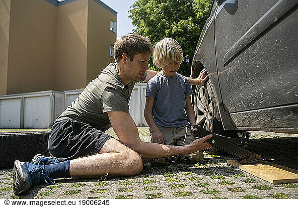 Boy watching father changing car tire in yard